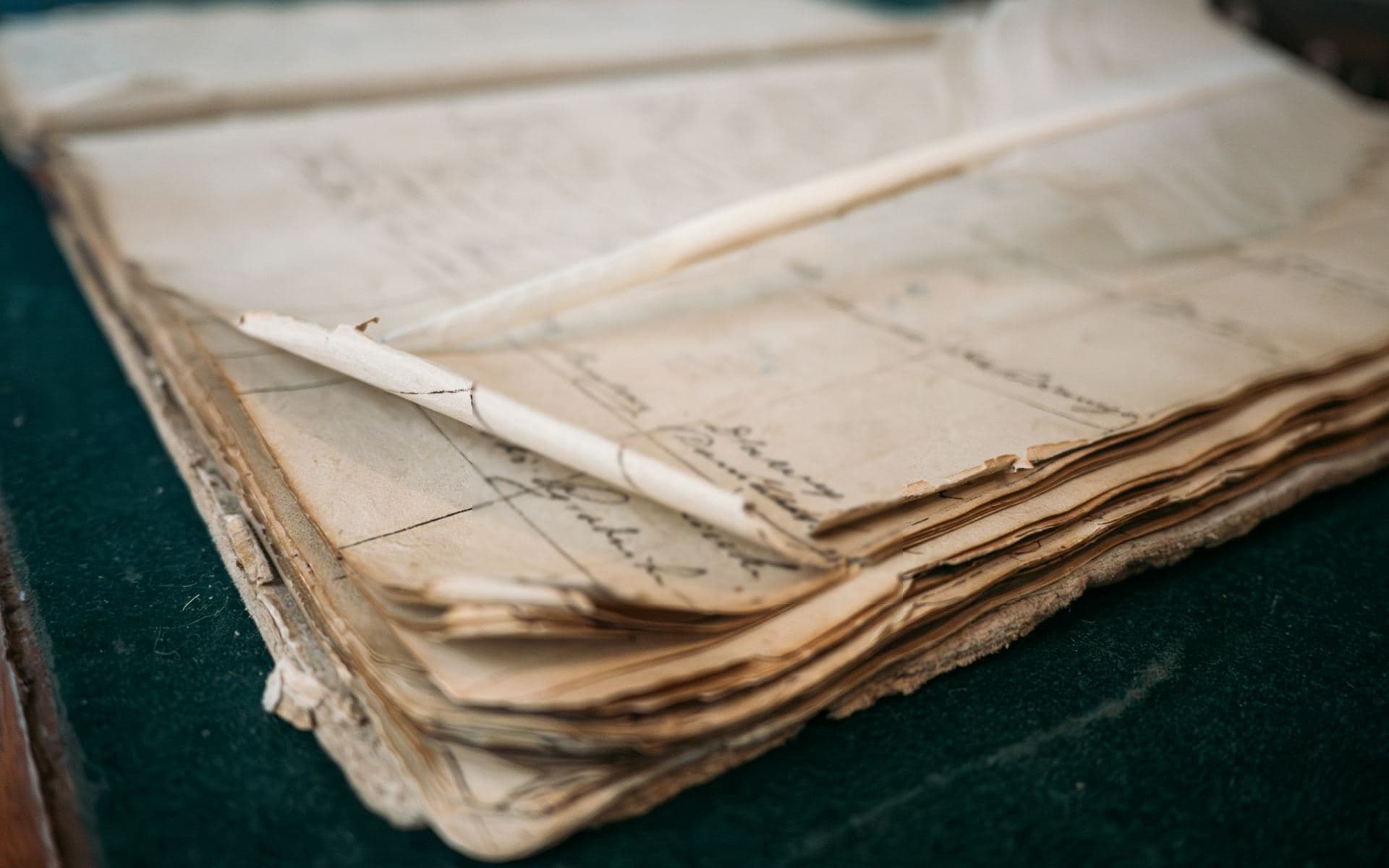 Ancien registre relié aux pages usées et plume posée dessus, sur un sous-main de feutre
