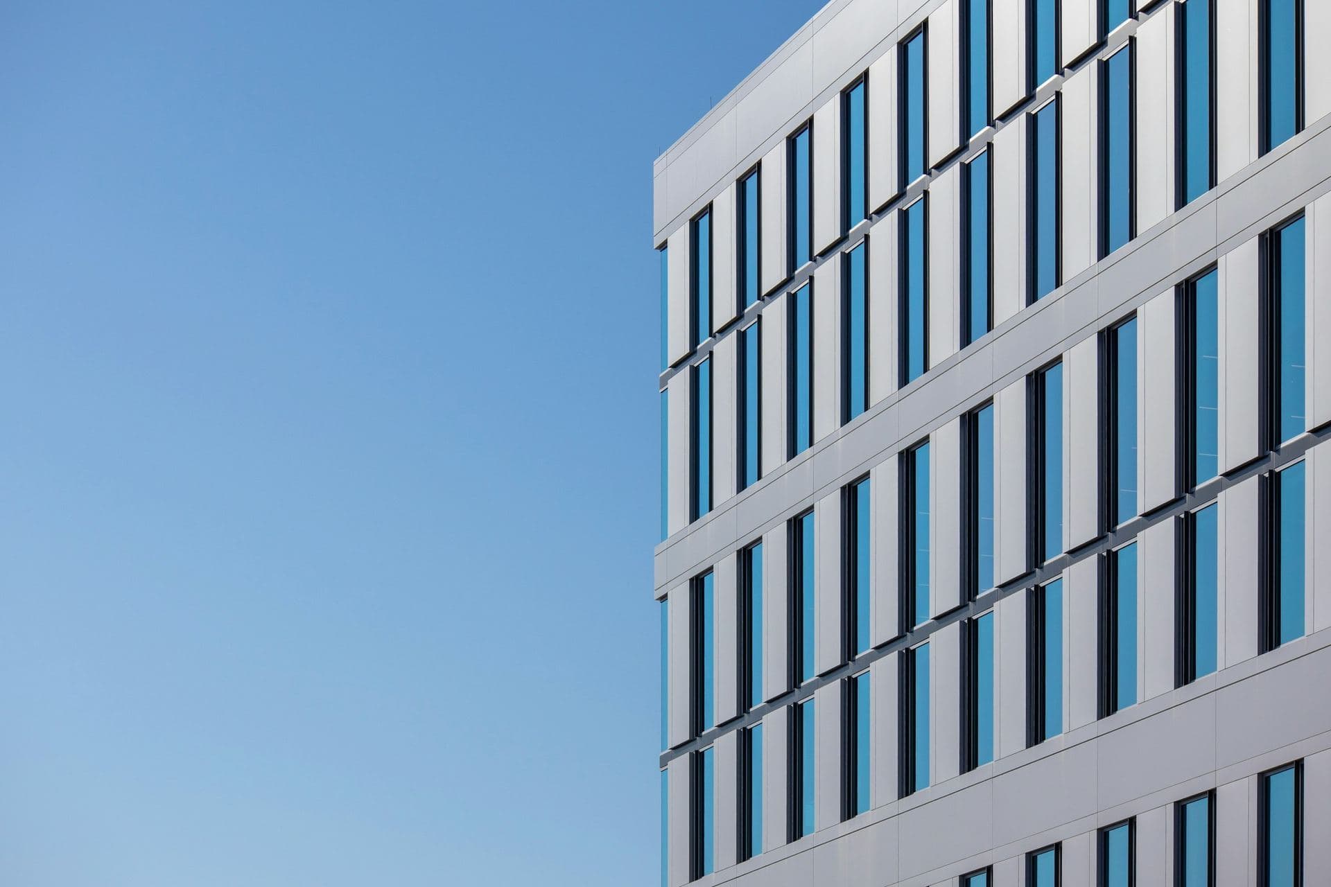 Façade d'immeuble de bureaux contemporain vue en contre-plongée, rythme de fenêtres verticales sur ciel uni